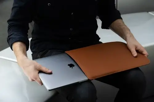 Man sitting on a bench and pulling a MacBook laptop from a case