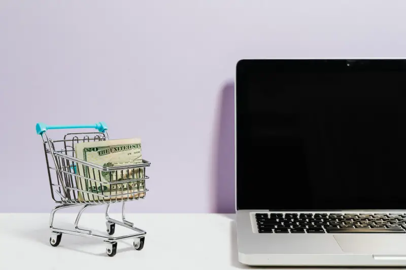 A shopping cart with cash beside laptop
